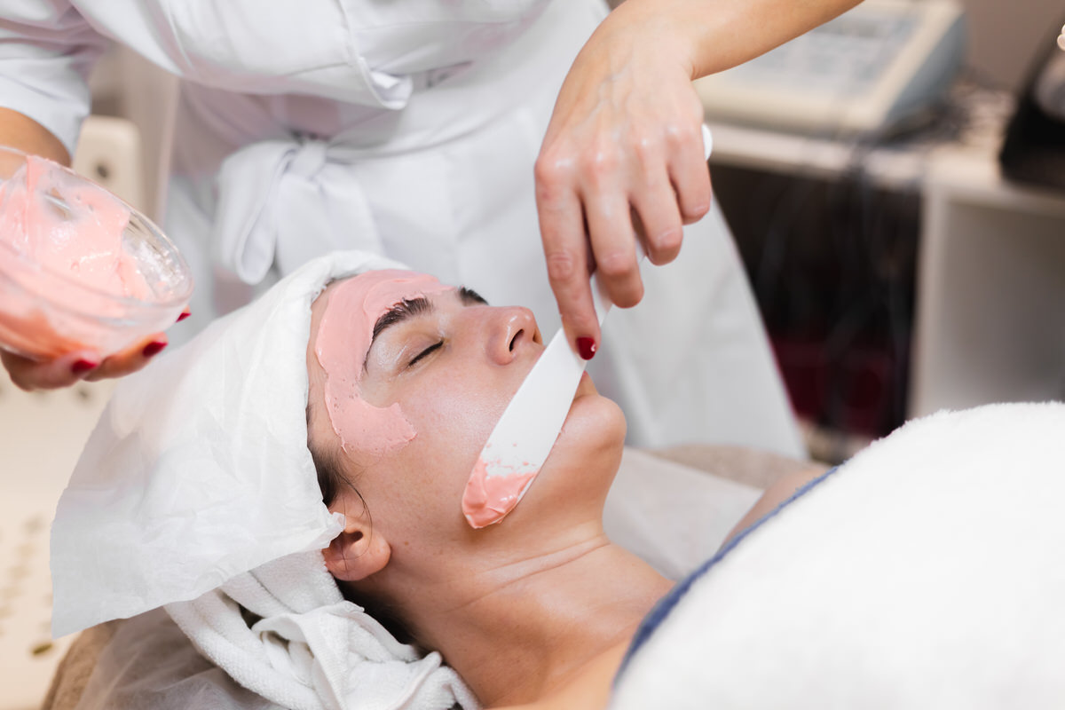 Cosmetologist applies alginate mask with spatula on face of woman. Facial skin and anti-aging treatment. Cosmetology and professional facial skin care. Cosmetologist applies alginate mask with spatula on face of woman. Facial skin and anti-aging treatment. Cosmetology and professional facial skin care.